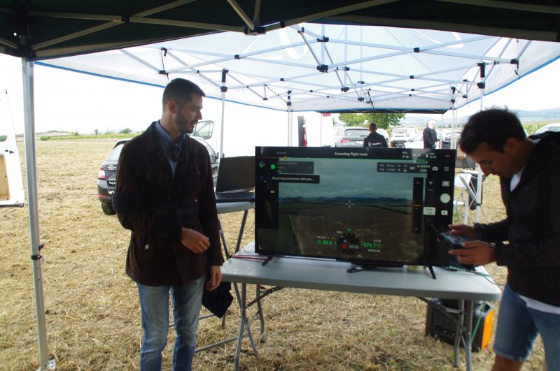 Dron DJI Mavic 3M letí nad zájmovou oblast a my můžeme sledovat jeho záběry na velkoplošné obrazovce. „Nad snímaným polem, které má uložené v ovladači sklopí kameru kolmo dolů. Zatažená obloha je pro