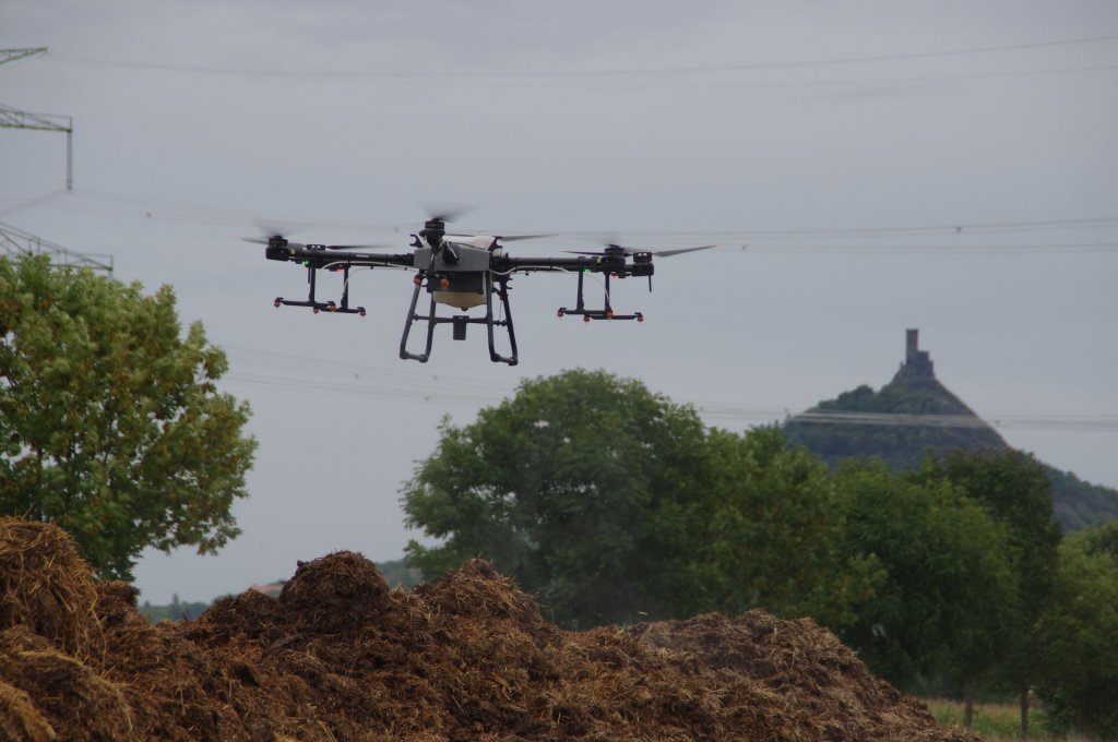Zemědělský dron DJI Agras T30 aplikuje variabilní dávku postřiku, větší na levou hromadu hnoje, menší na tu pravou. V nádrži má vodu