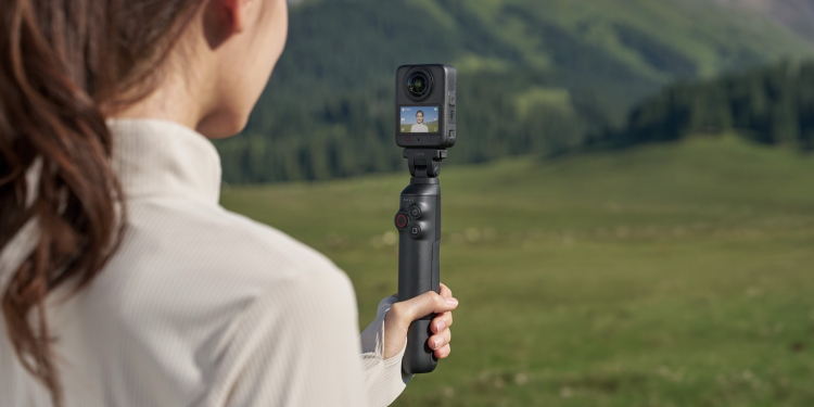 DJI Osmo 360 II na selfie tyči v ruce, v pozadí zelené kopce