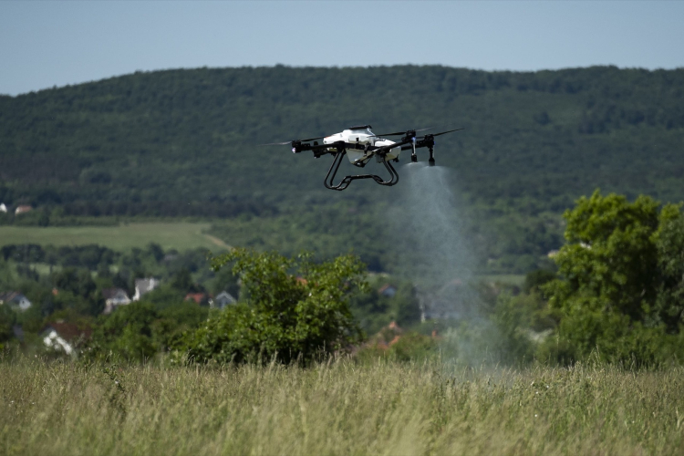Postřikový DRON ABZ Innovation při postřiku louky, v pozadí zalesněné kopce